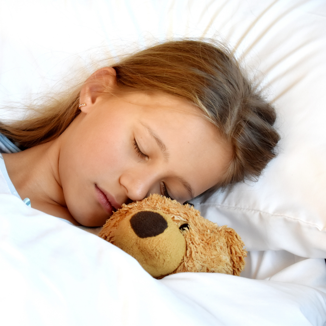 close up of young girl sleeping in bed next to teddy bear