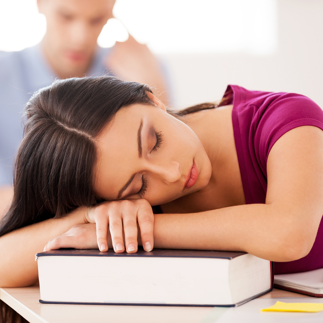 woman in pink top with folded arms sleeping on text book